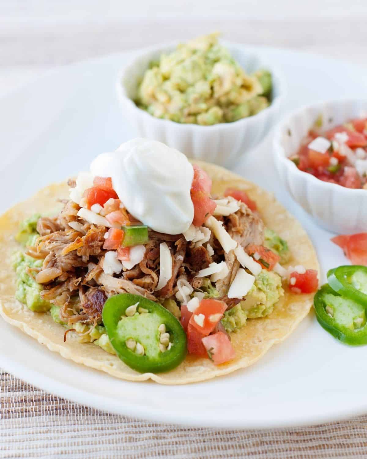 pork carnitas served in a tostada and topped with jalapeño slices, pico de gallo and sour cream