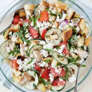 a bowl of panzanella salad with cucumber, tomato and crumbled cheese