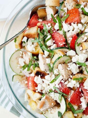 close up of a bowl of panzanella salad with cucumber, tomato and crumbled cheese