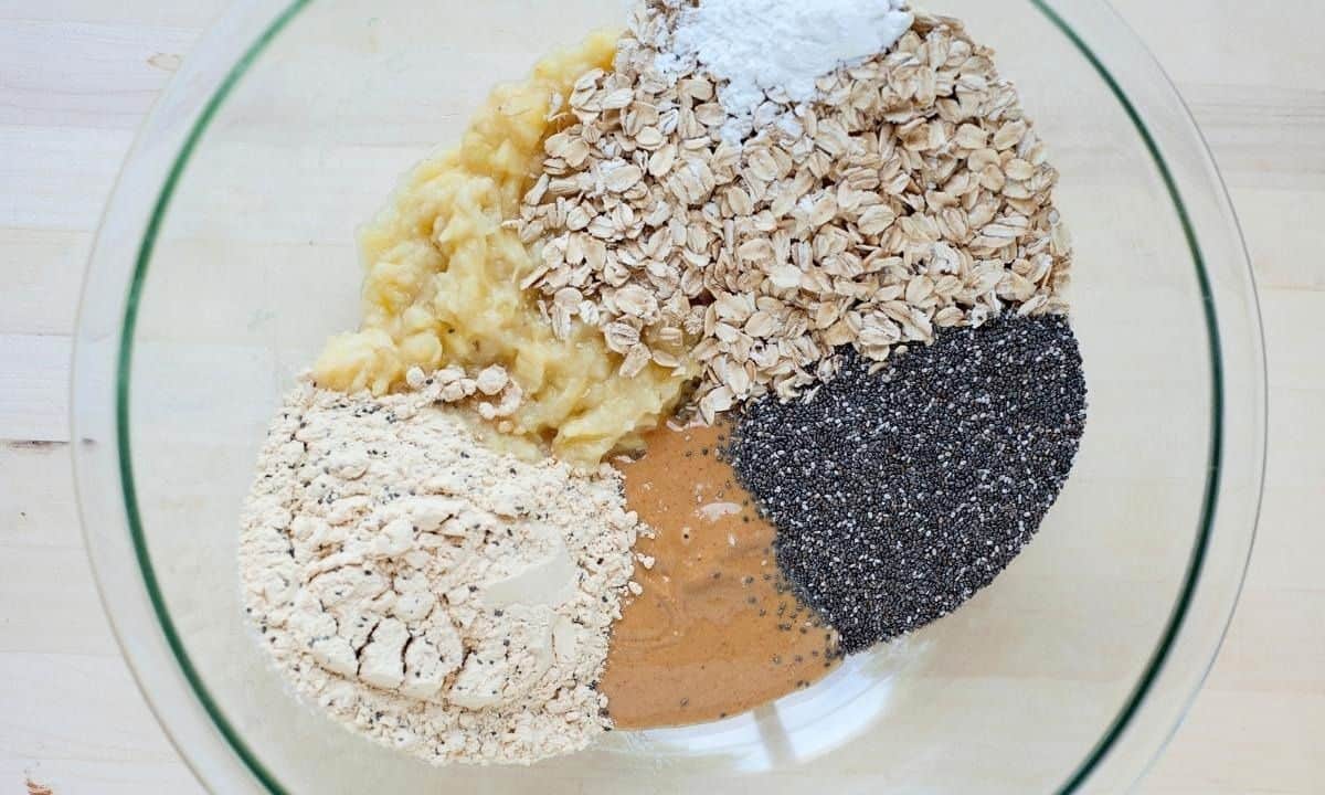 bowl with ingredients to make oatmeal protein cookies: bananas, oats, protein powder, peanut butter, chia seeds, baking powder