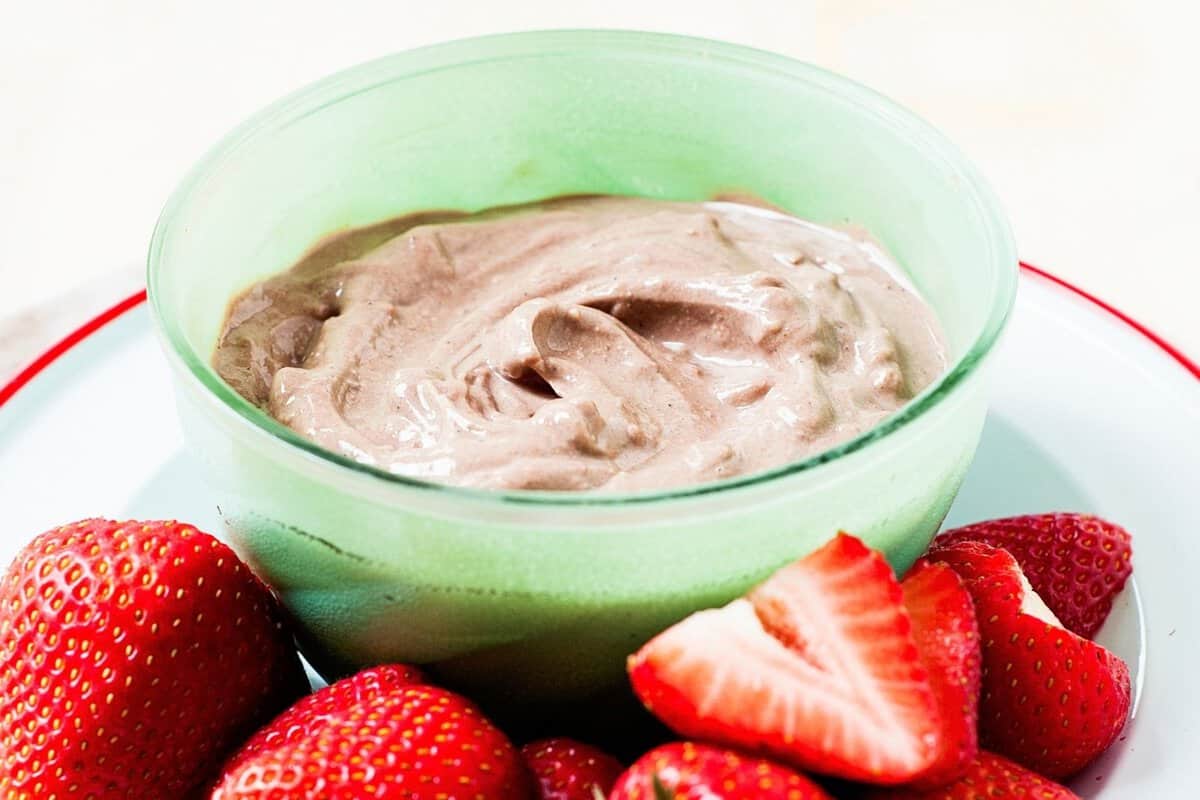 A small bowl with chocolate peanut butter yogurt dip on a plate with strawberries on the side