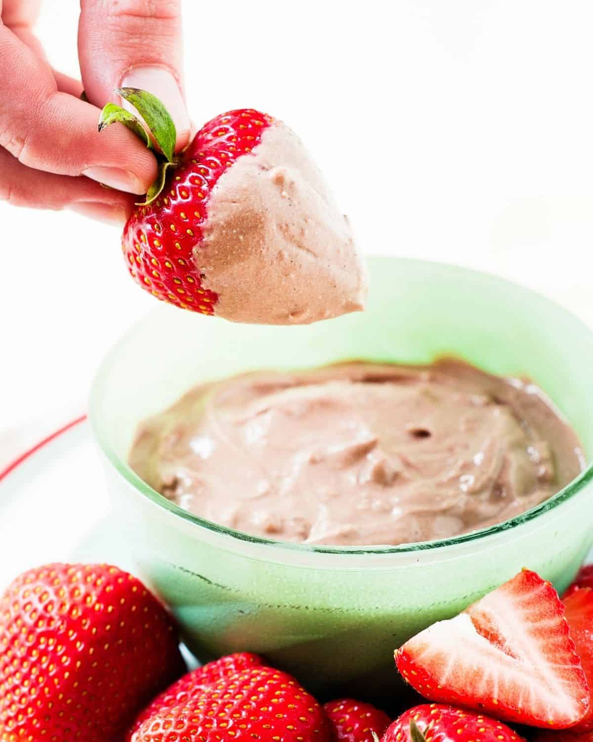dipping a strawberry in a small bowl with chocolate peanut butter yogurt dip