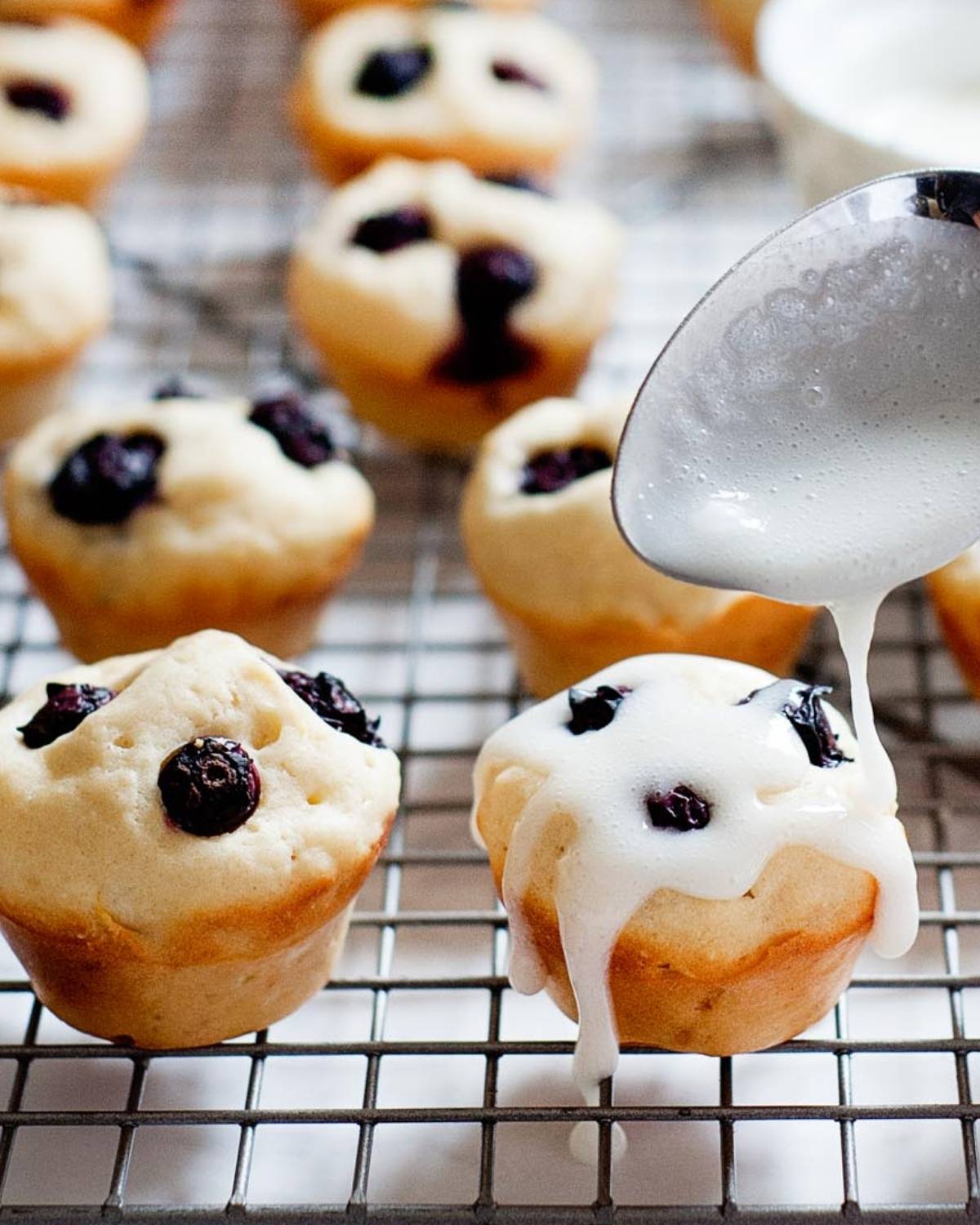 drizzling a simple powdered sugar glaze over blueberry pancake bites on a cooling rack.