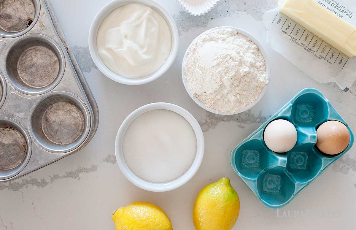 a muffin pan, eggs, lemons, butter, and bowl with sugar, flour, and greek yogurt