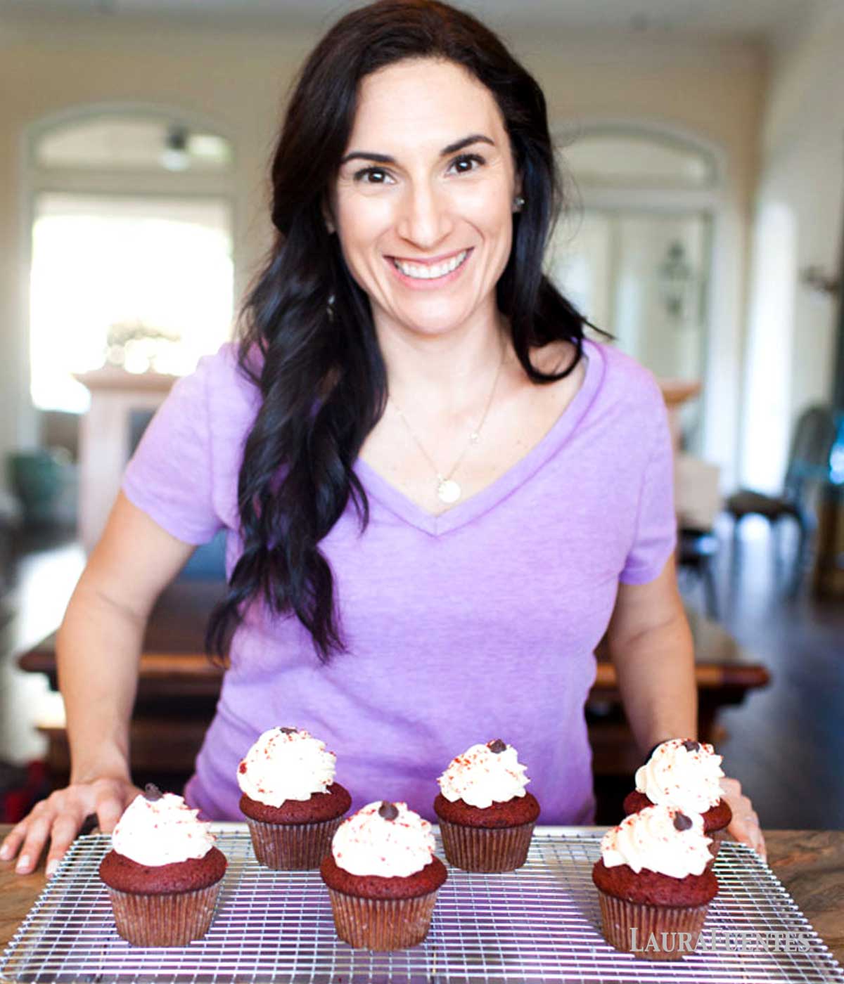 laura fuentes standing next to a cooling rack with five red velvet cupcakes
