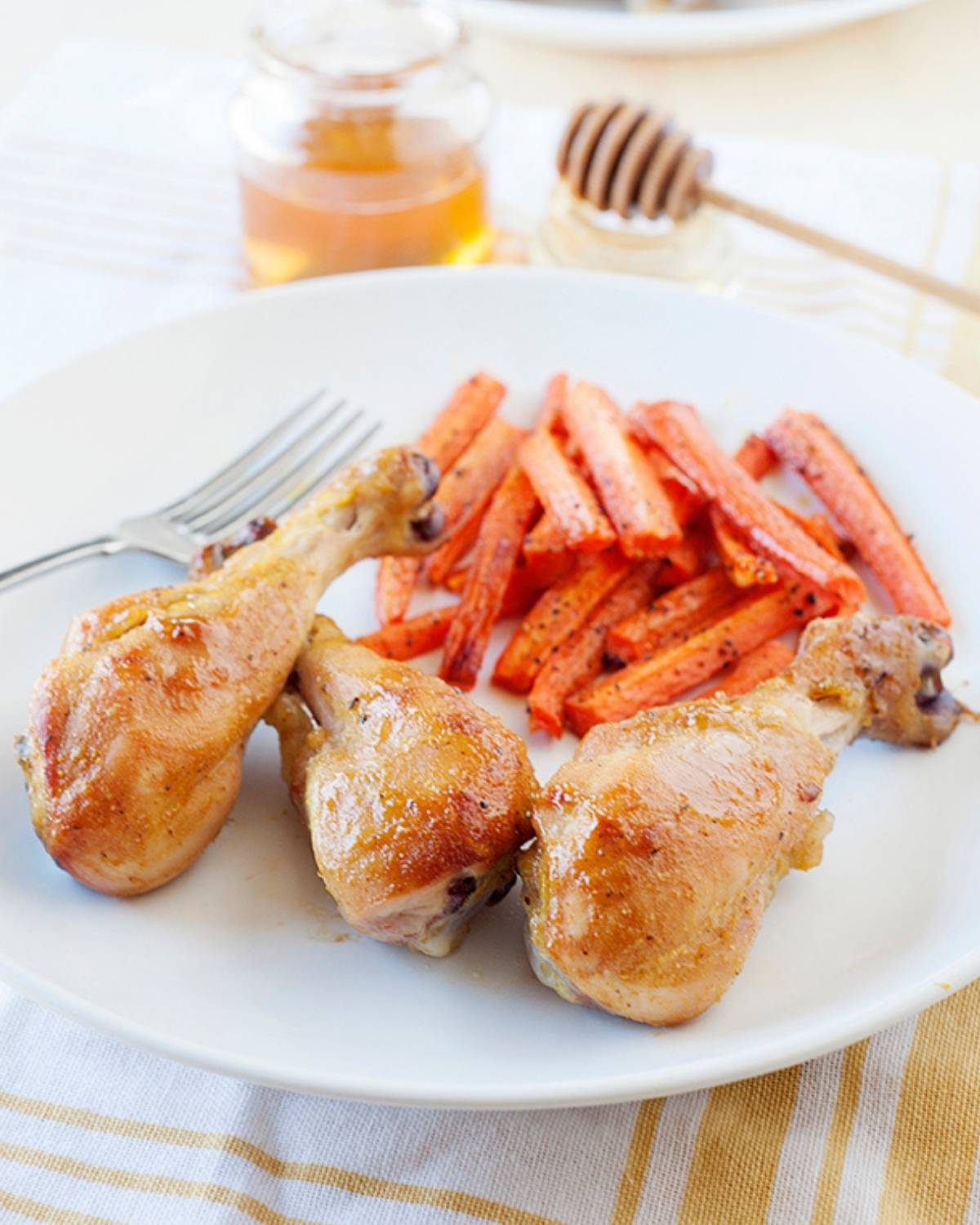 three honey chicken legs on a plate with carrot fries