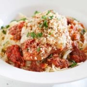 Slow-cooker chicken parmesan over pasta in a white bowl