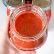 a hand showing a jar of tomato sauce