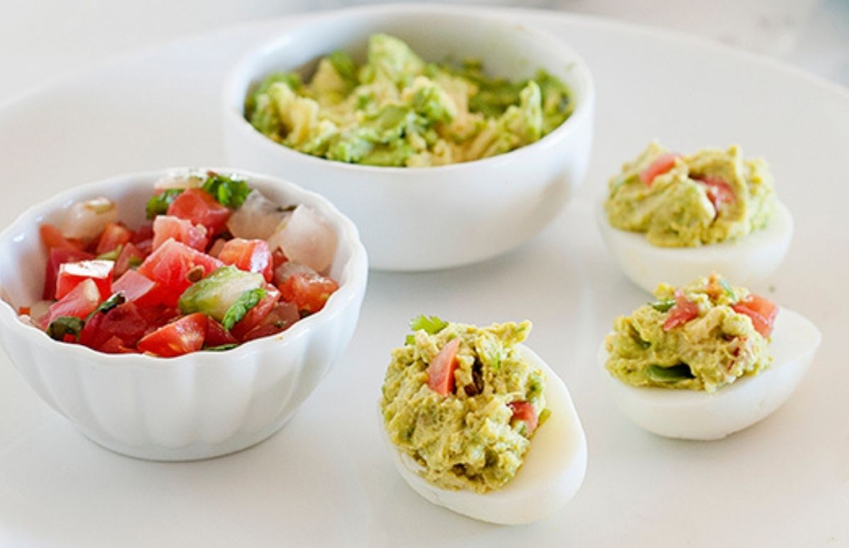 Guacamole deviled eggs on a large plate with two dips