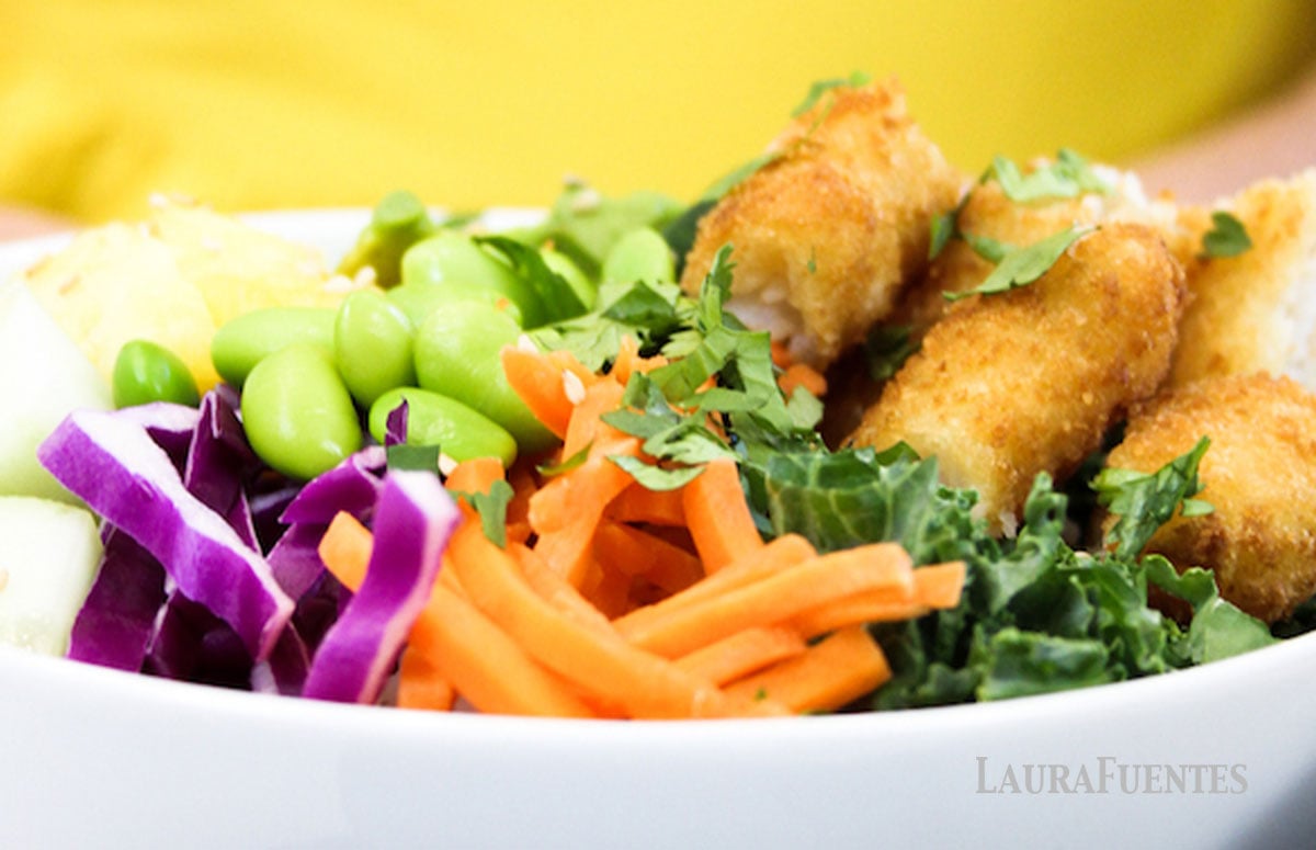 crunchy breaded fish poké bowl with chopped pineapple, sliced cucumber, matchstick carrots, sliced avocado, chopped kale, edamame beans, cooked rice
