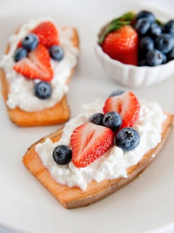 sweet potato toast topped with cottage cheese and berries, and a small bowl of berries on the side