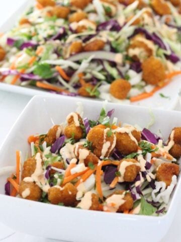 a bowl with popcorn shrimp salad with dressing and more salad behind on a platter