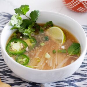 white bowl of homemade pho with cilantro, sliced jalapeño and a lime wedge