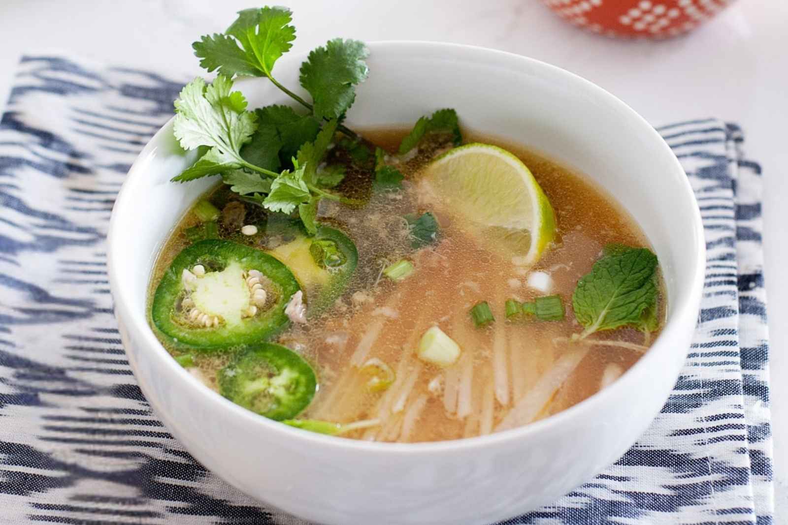 white bowl of homemade pho with cilantro, sliced jalapeño and a lime wedge
