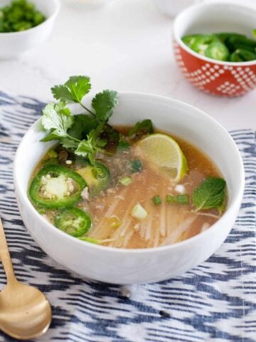 white bowl of homemade pho with cilantro, sliced jalapeño and a lime wedge