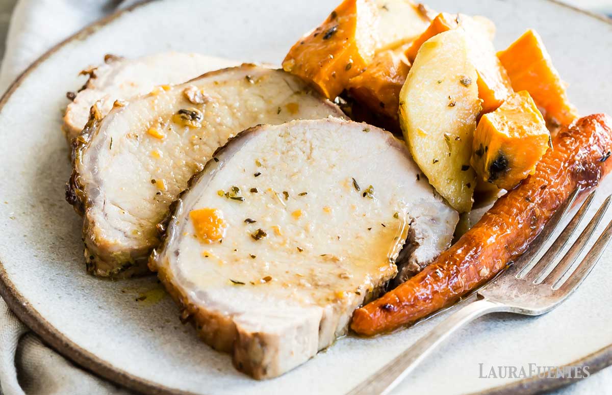 two slices of baked pork with a brown sugar and dijon glaze with sweet potatoes and carrots on a white plate