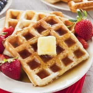 two buttermilk waffles on a plate topped with some butter and syrup with strawberries on the side.
