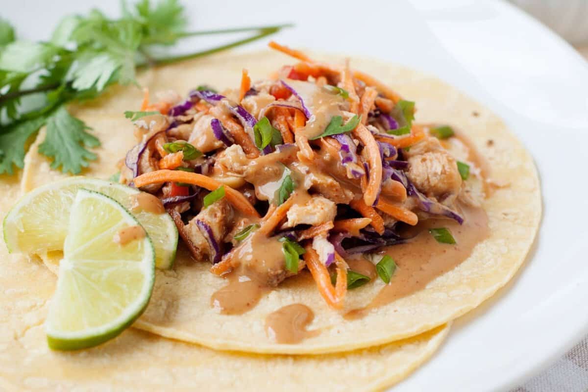 thai chicken taco with peanut sauce and lime wedges on the side