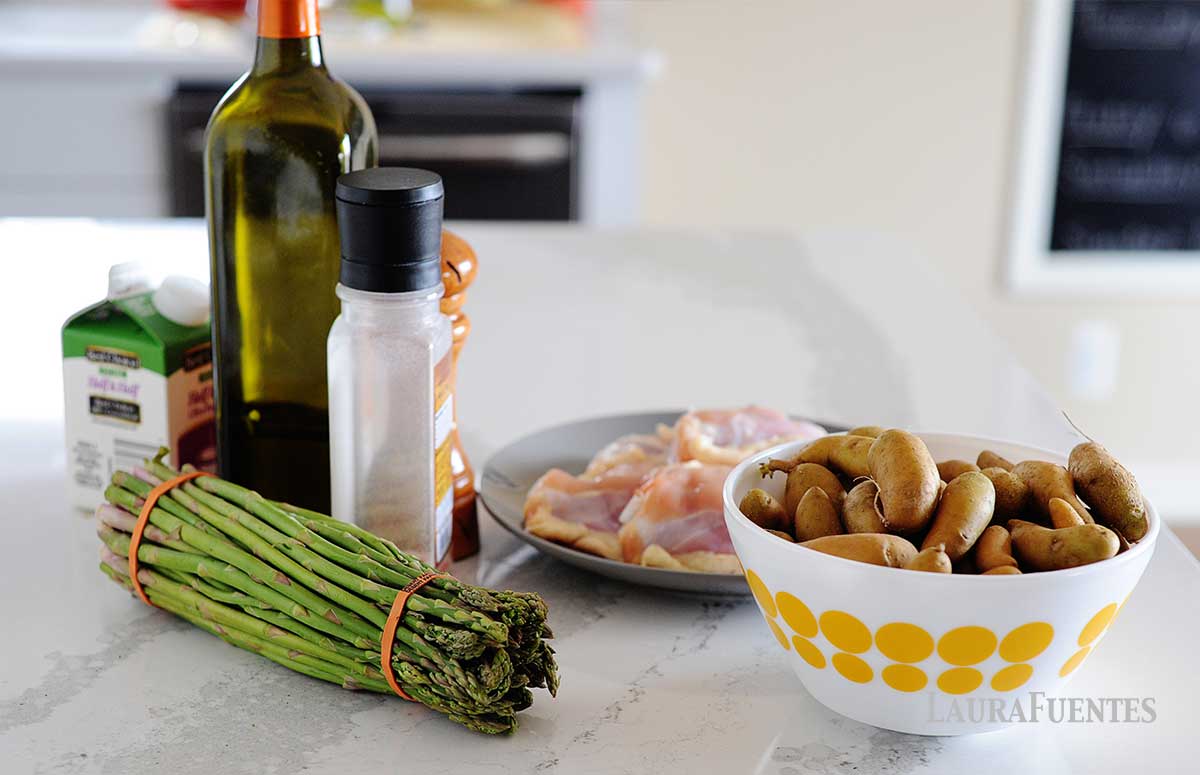 sheet pan chicken and potatoes ingredients on a kitchen counter: potatoes, raw chicken, a bottle of olive oil, asparagus, salt and pepper