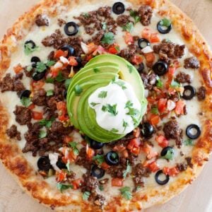 overhead view of taco pizza with avocado and sour cream on top