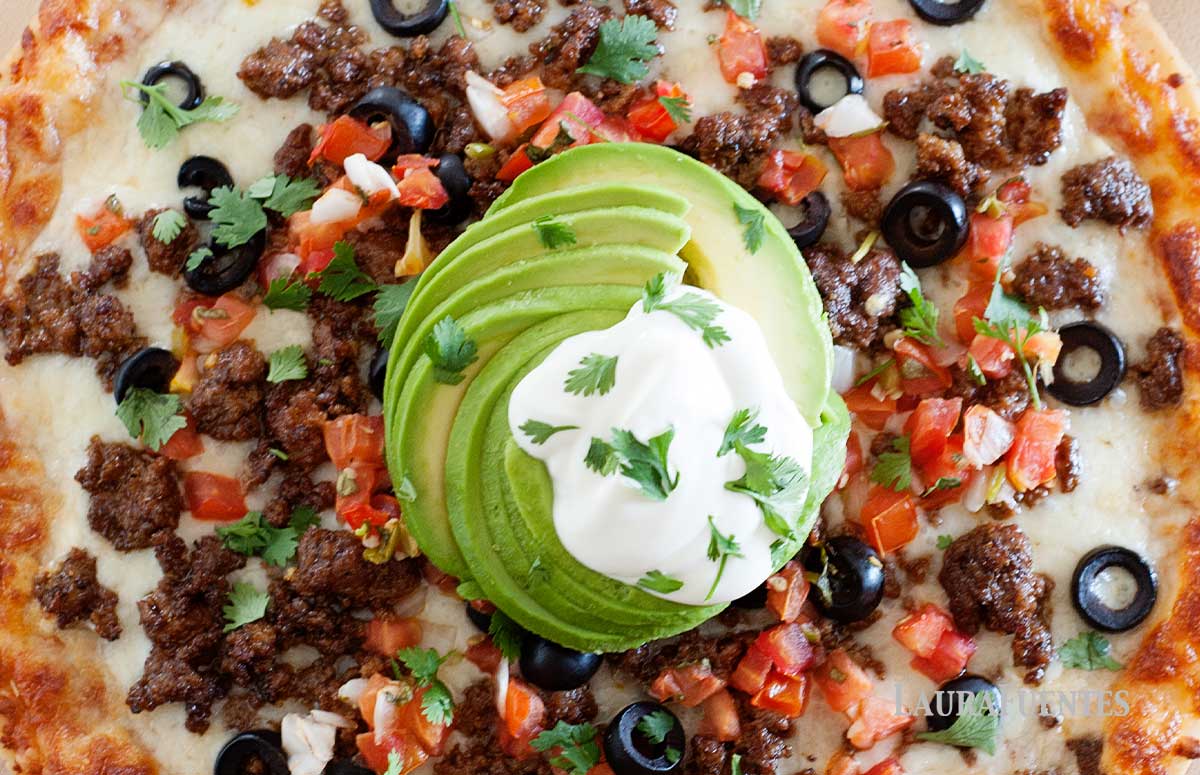 overhead view of taco pizza with avocado and sour cream on top