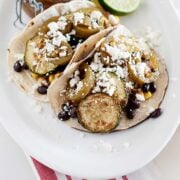 two blackened zucchini tacos on a plate with lime