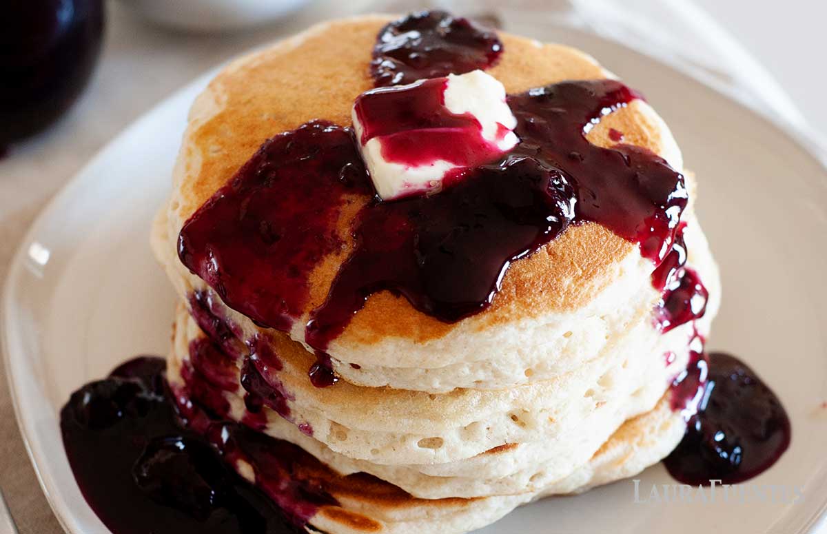 A stack of pancakes on a plate with homemade blueberry syrup and butter on the top
