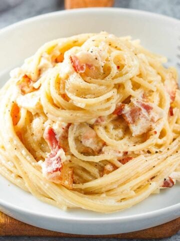 close up view of spaghetti carbonara with pieces of bacon on a plate