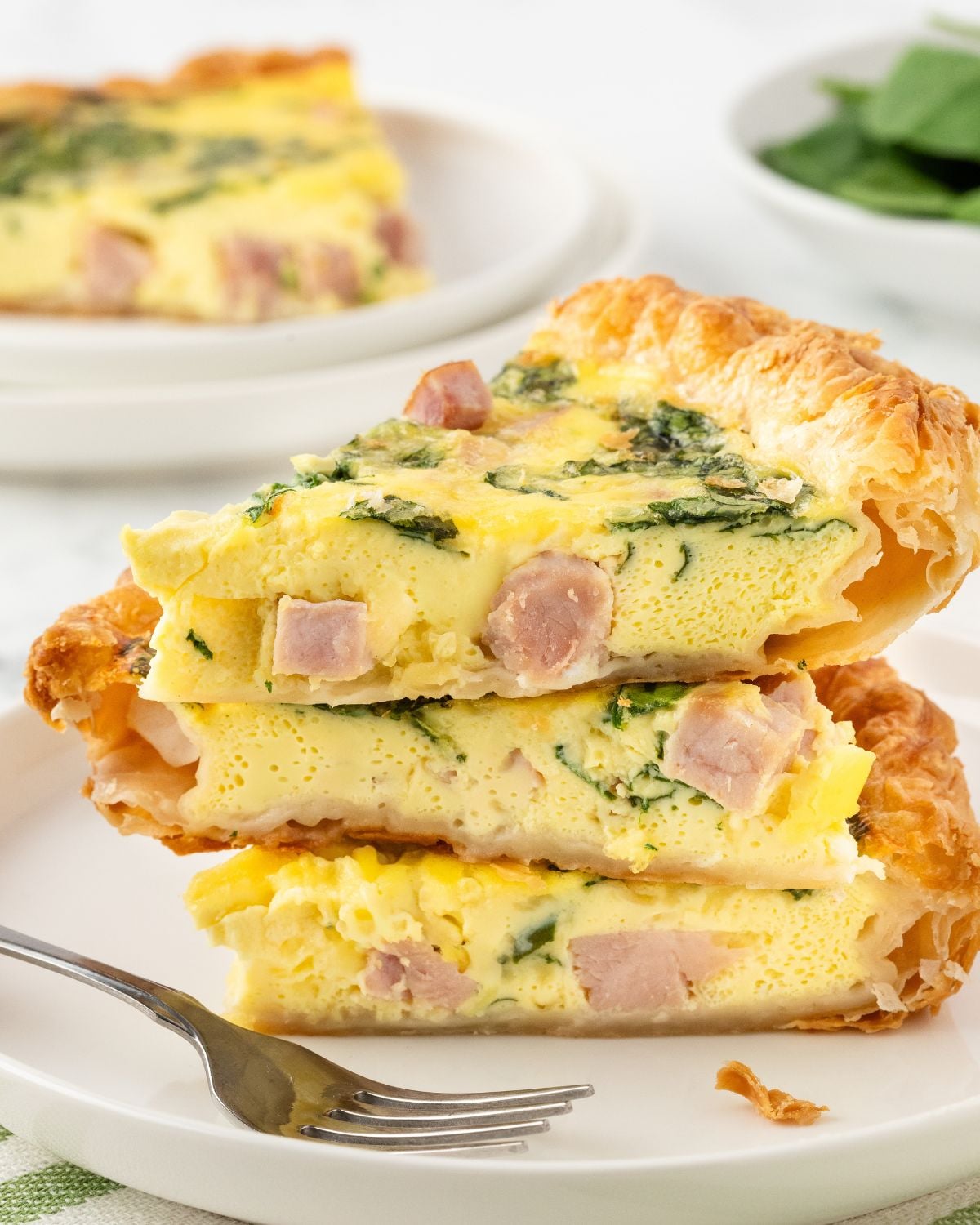 three slices of puff pastry quiche stacked on top of each other to show the filling made with ham, cheese, and spinach.