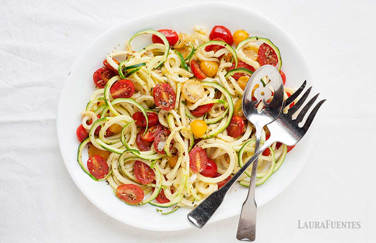 zucchini noodles on a plate with spices and halved tomatoes