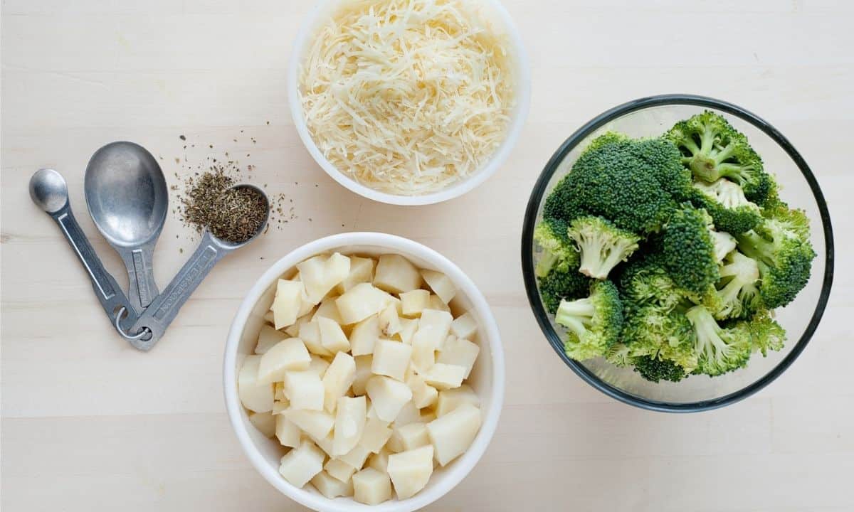 three bowls with broccoli, cooked potatoes, grated cheese, and measuring spoons with seasonings