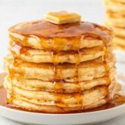 stack of homemade fluffy pancakes from scratch stacked on a plate, topped with a pat of butter, and pancake syrup over the top
