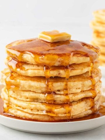 stack of homemade fluffy pancakes from scratch stacked on a plate, topped with a pat of butter, and pancake syrup over the top