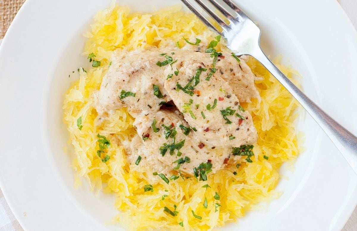 bed of spaghetti squash on a white plate with chicken in garlic butter on top