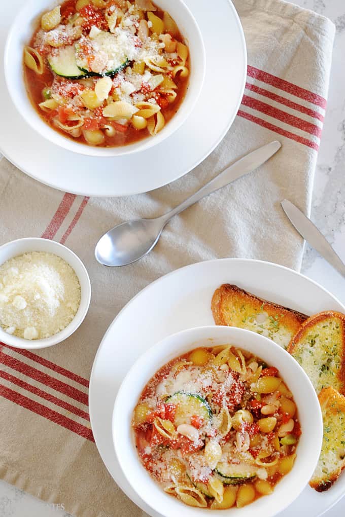 overhead look at two large bowls of minestrone soup. Small dish of Parmesan cheese to one side