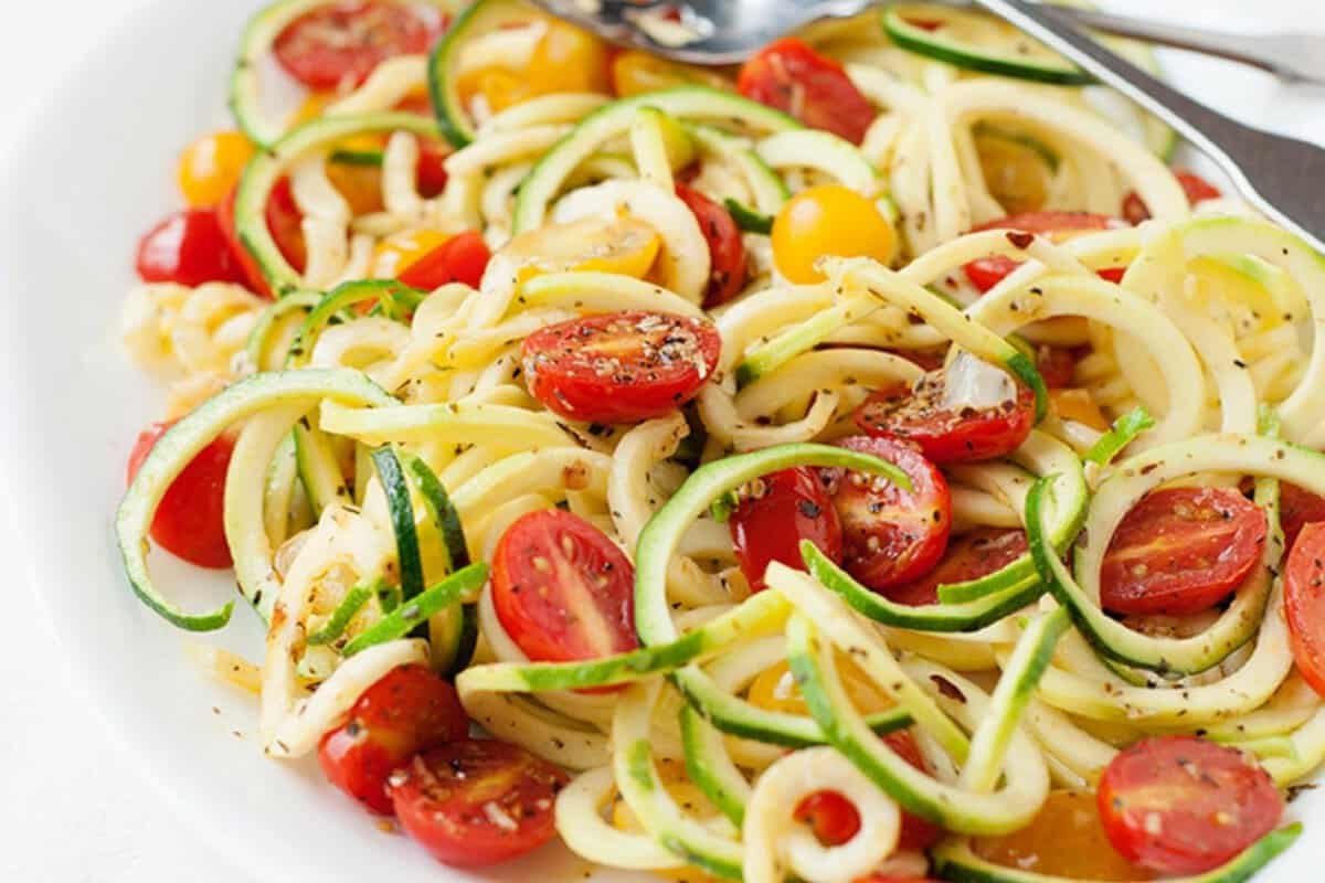 zucchini noodles on a plate with spices and halved tomatoes