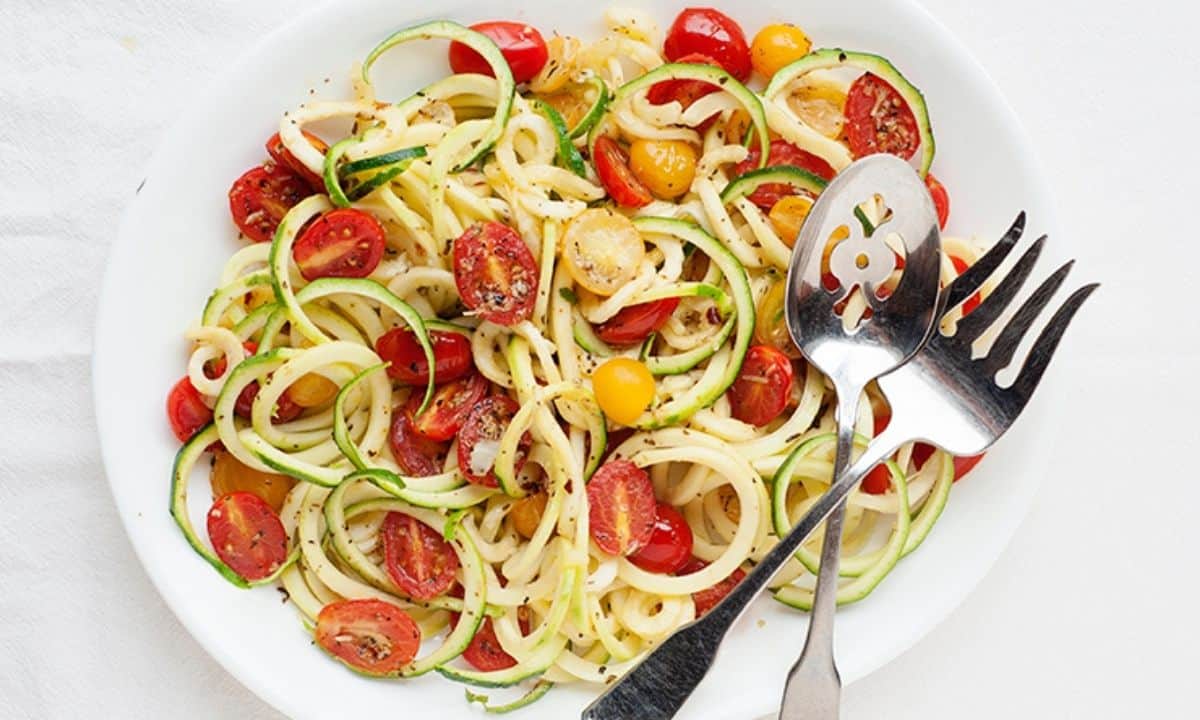 overhead view of zucchini noodles on a plate with spices and halved tomatoes