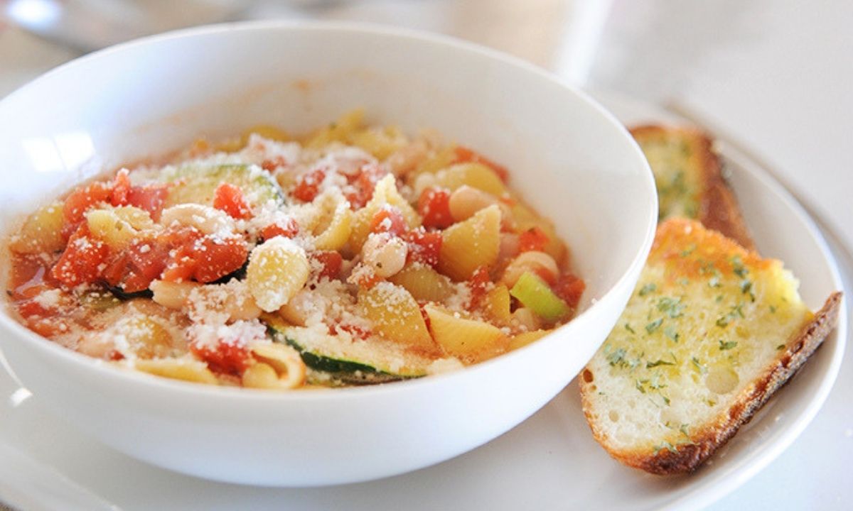 a white bowl with minestrone soup with bread on the side