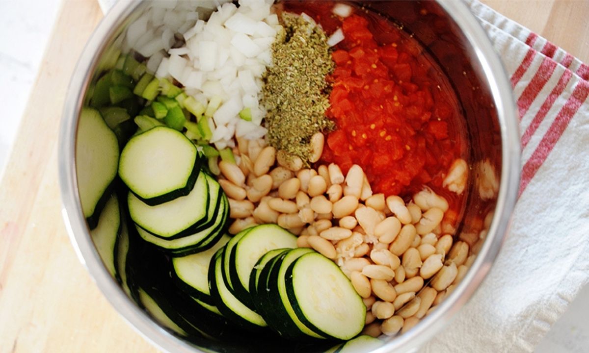 a bowl with minestrone soup ingredients: zucchini, white beans, tomato, onion, celery and seasonings