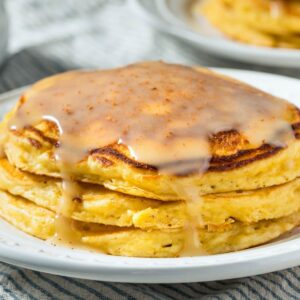 stack of fluffy eggnog pancakes on a plate topped with a syrup glaze