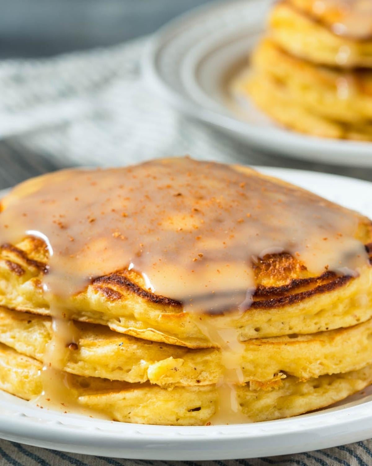 stack of fluffy eggnog pancakes on a plate topped with a syrup glaze