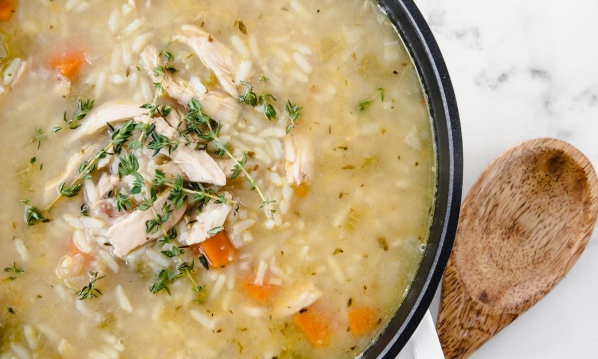 large pot of chicken and rice soup and a wooden spoon on the side