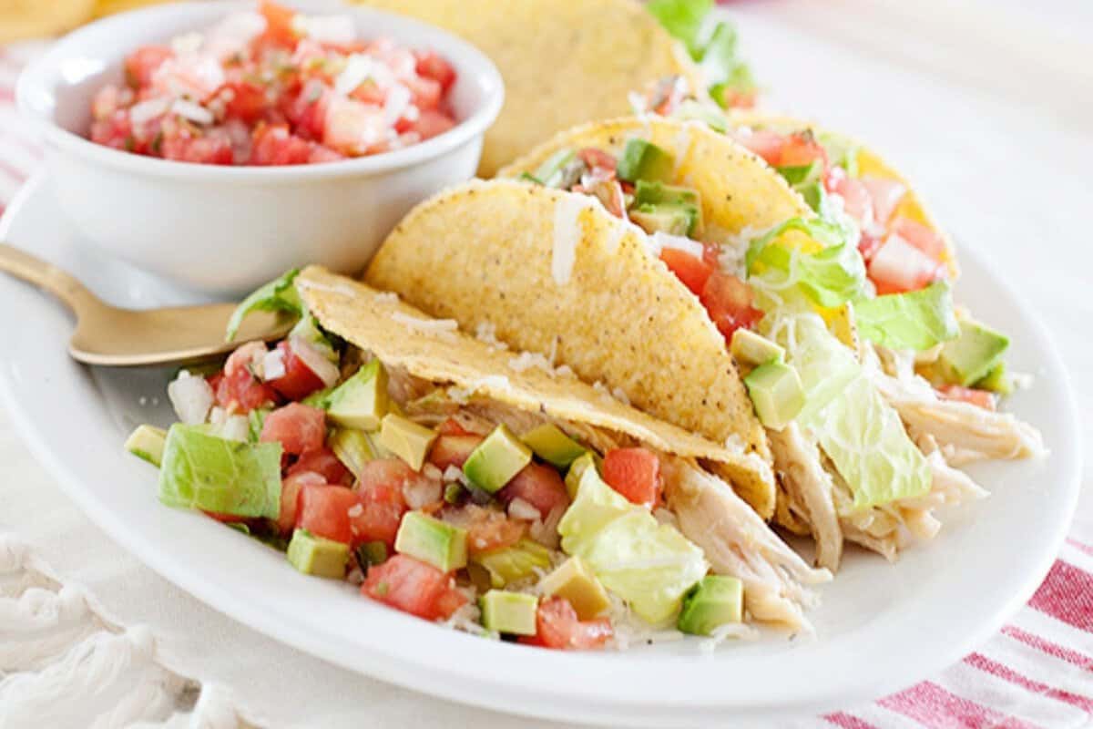 Slow Cooker Salsa Verde Chicken Tacos on a white plate and a small bowl of pico de gallo on the side