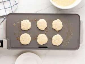 griddle with six raw pancakes