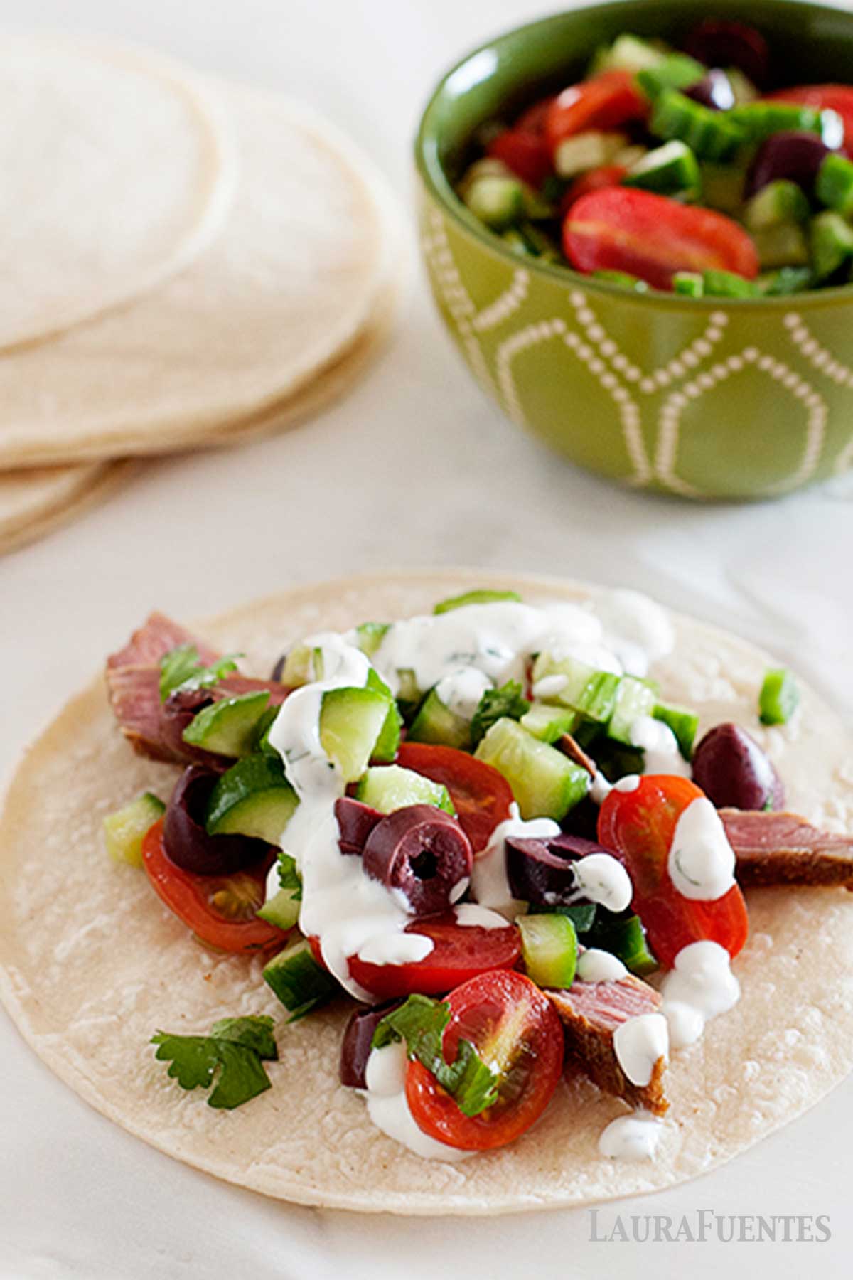 greek tacos with cucumber tacos on a plate with more tacos in the background