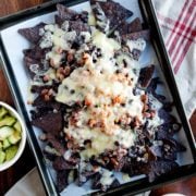 homemade nachos on a cooking tray with avocados and salsa on the side