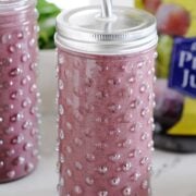 Two glass jars of purple smoothies with jar of prune juice in the background.