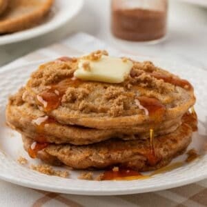 stack of cinnamon pancakes on a plate topped with a little butter, brown sugar, and pancake syrup