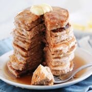 large stack of cinnamon pancakes topped with butter and syrup with one bite taken out
