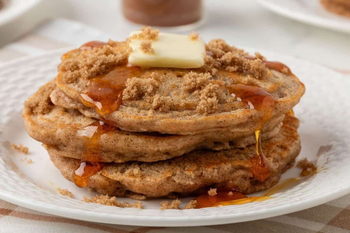 stack of cinnamon pancakes on a plate topped with a little butter, brown sugar, and pancake syrup